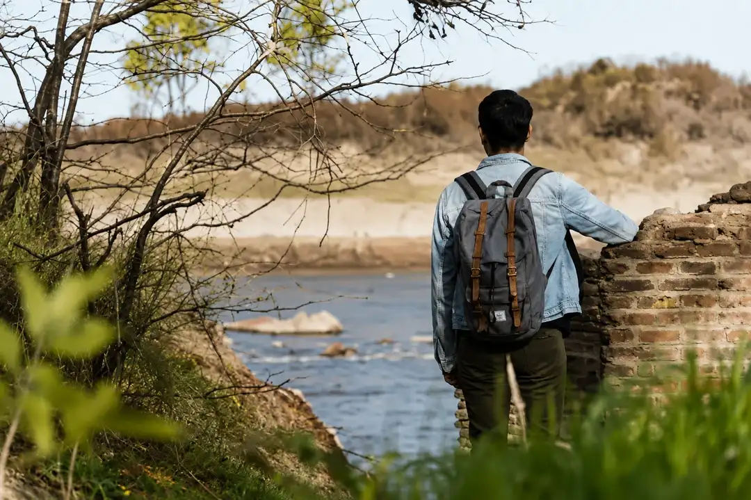 Man with a survival backpack looking at a river from the shore